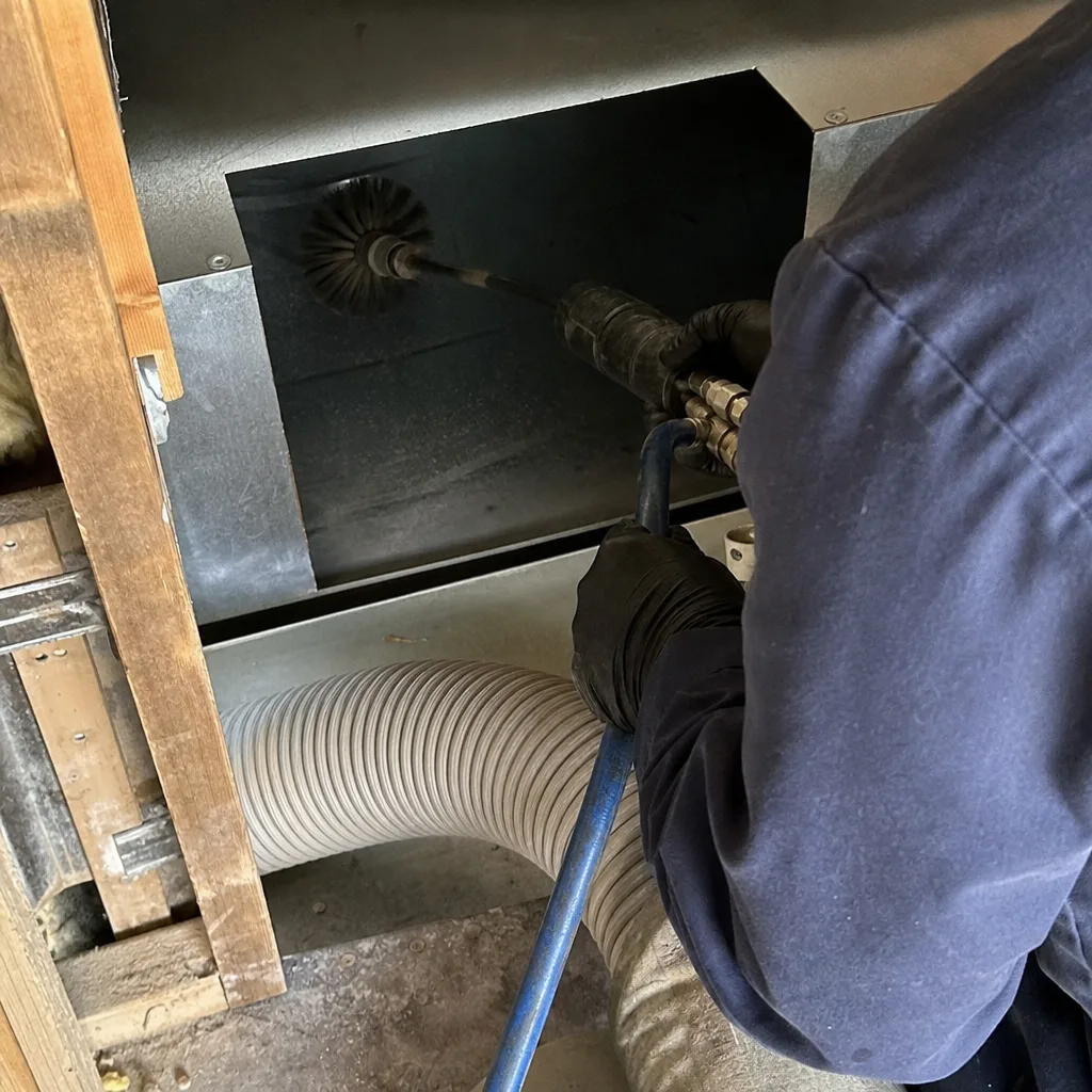 Professional air duct cleaning technician using a rotating brush tool